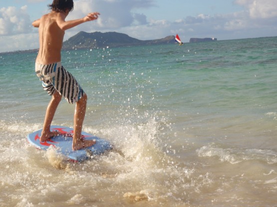Finn skimboarding on the boogie board - in the background you can see an outrigger canoe with a sail: this is pretty much how the Polynesians came here 1000 years ago
